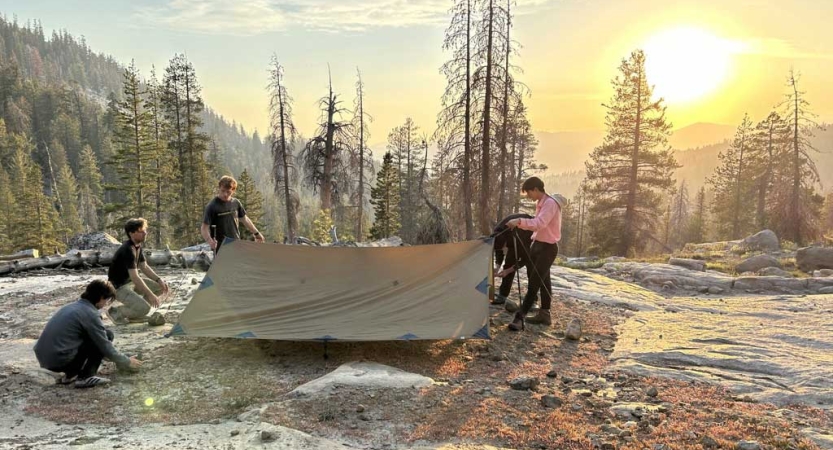 a group of outward bound students work to set up tarp shelters 